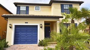 A two-story house with a blue garage door, a small window, and a door with a light fixture above it. - 5439 Solterra House 5 Bedroom by Florida Star (Davenport)