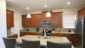 A modern kitchen with granite countertops, stainless steel appliances, and wooden cabinets. - 5439 Solterra House 5 Bedroom by Florida Star (Davenport)