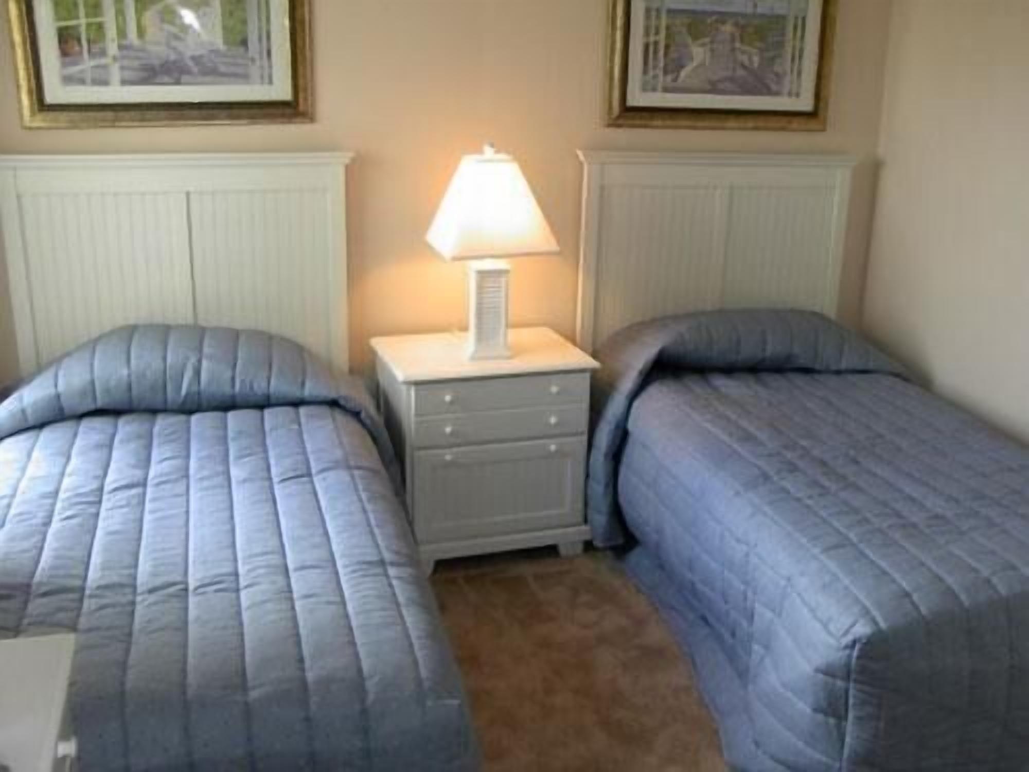 A room with two single beds, a nightstand with a lamp, and framed pictures on the wall.