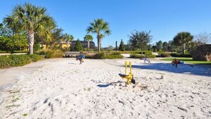 A sandy beach area with playground equipment and palm trees.