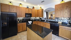 A kitchen with wooden cabinets, a black refrigerator, a microwave, and a black countertop island.