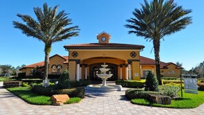 A yellow building with a clock tower, palm trees, and a fountain in the center.