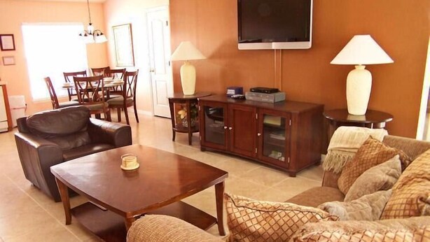 Un salon comprenant un canapé, une table basse, un téléviseur fixé au mur et un coin repas avec des chaises et une table.