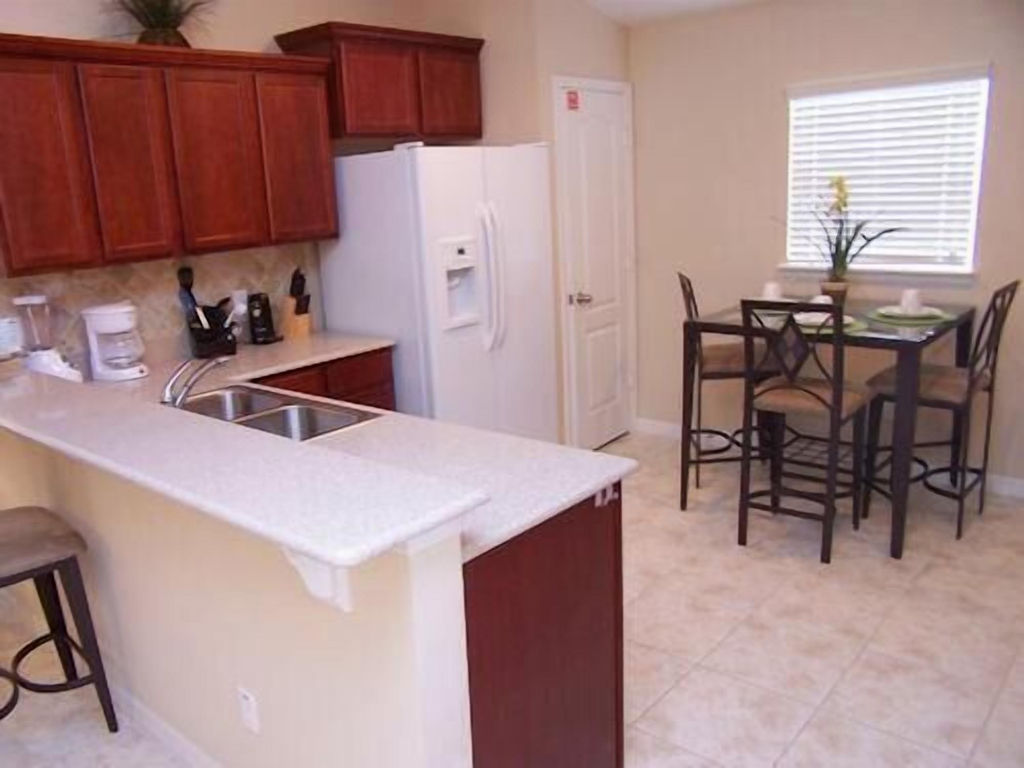 A kitchen with wooden cabinets, a white refrigerator, a sink, and a dining area with four chairs and a table.