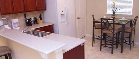 A kitchen with wooden cabinets, a white refrigerator, a sink, and a dining area with four chairs and a table.