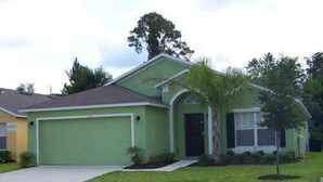 A single-story house with a green garage, a small front yard with a palm tree, and a clear sky.