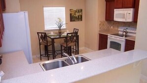 A compact kitchen with a sink, a dining table with chairs, a microwave, and cabinets.