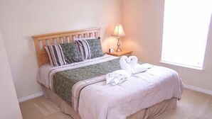 A neatly made bed with a wooden headboard, a bedside lamp, and a window with daylight.