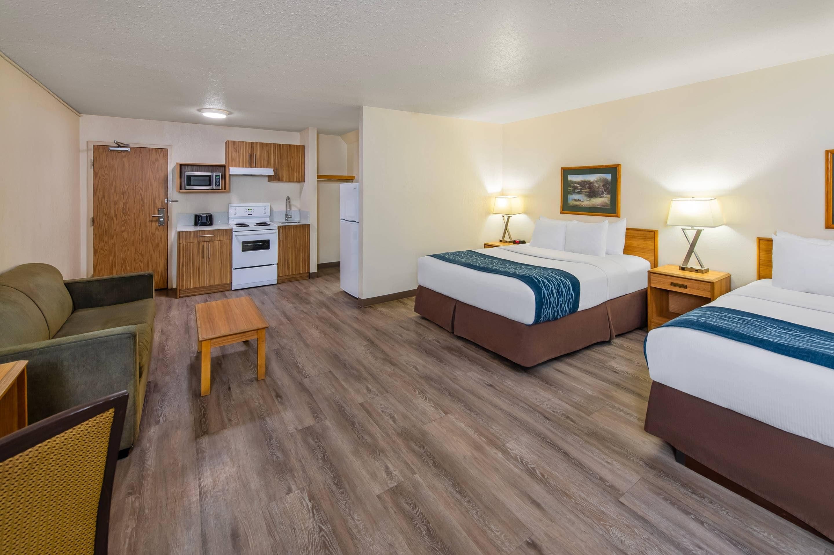 A hotel room with two beds, a kitchenette, a dining area, and a view of the outdoors.