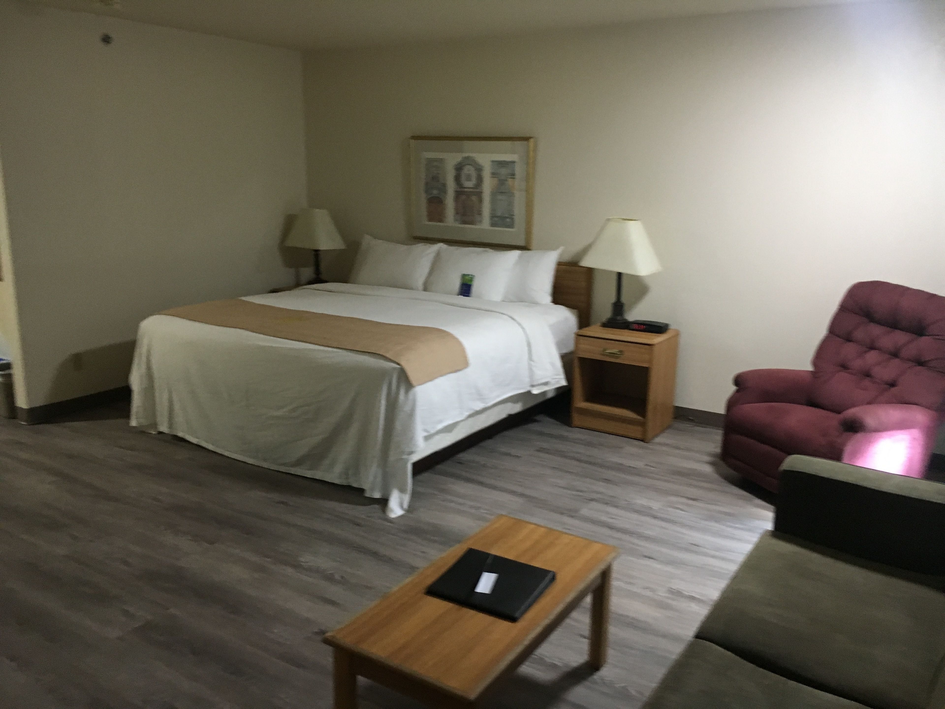 Een hotelkamer met een bed, nachtkastjes, een stoel en een kleintje tafeltje.