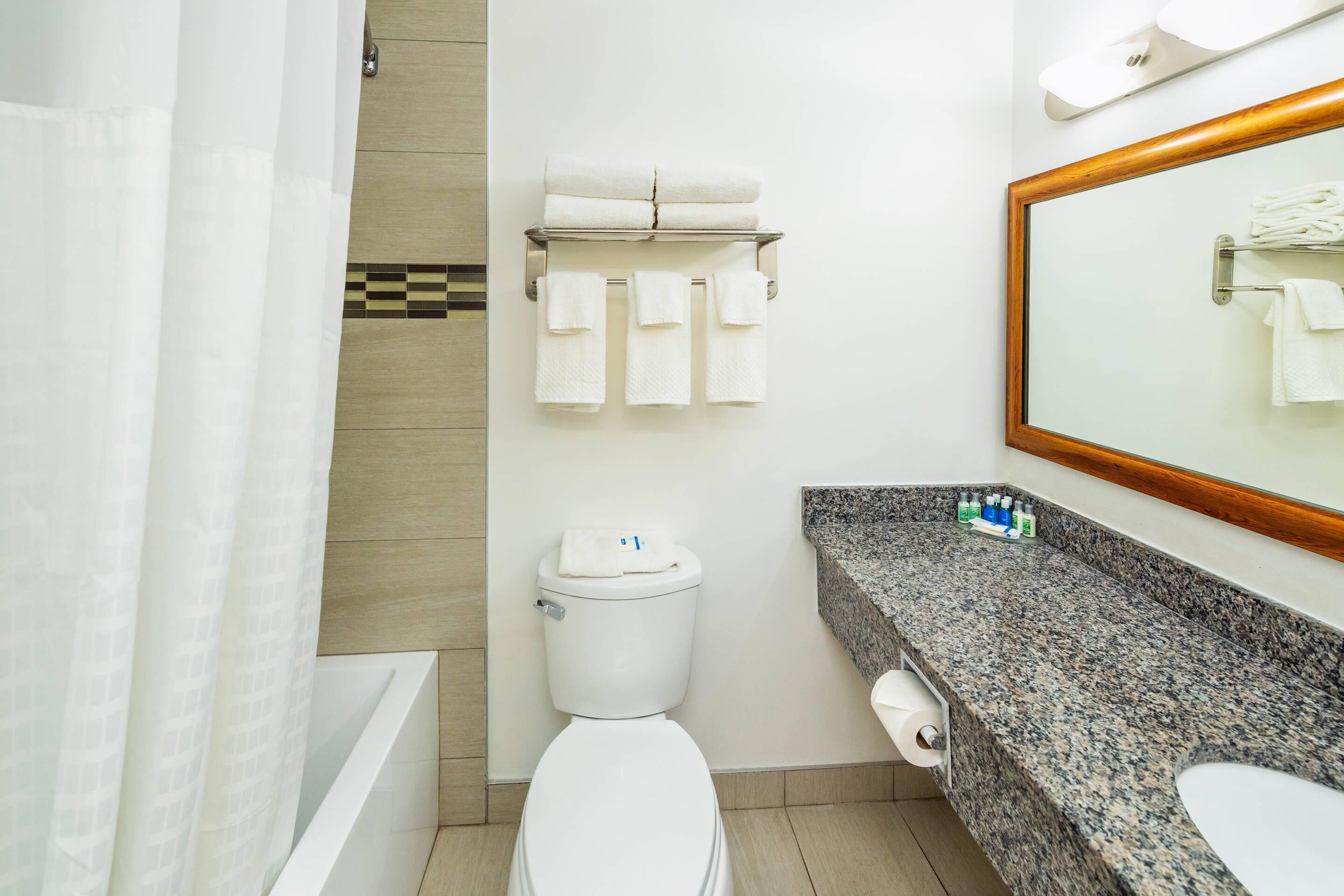 A modern bathroom with a toilet, a sink with a granite countertop, and a towel rack with multiple towels.