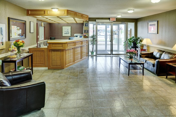 A lobby with a reception desk, a seating area with a couch and a coffee table, a large potted plant, and a glass door leading outside. - Rodeway Inn (Edson)