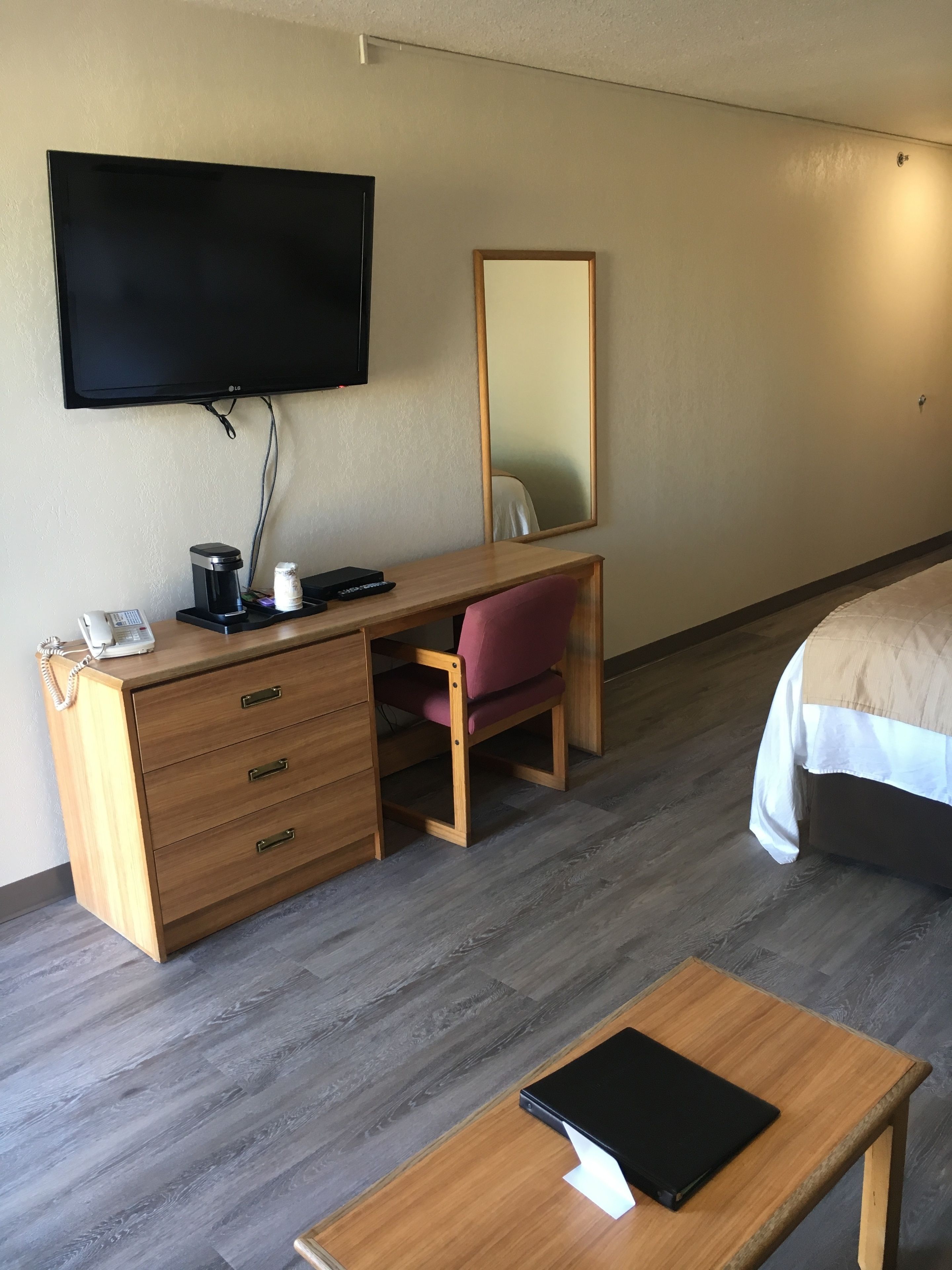 Une chambre d’hôtel avec un bureau en bois, une chaise, un lit, une télévision, un miroir et une table de chevet.