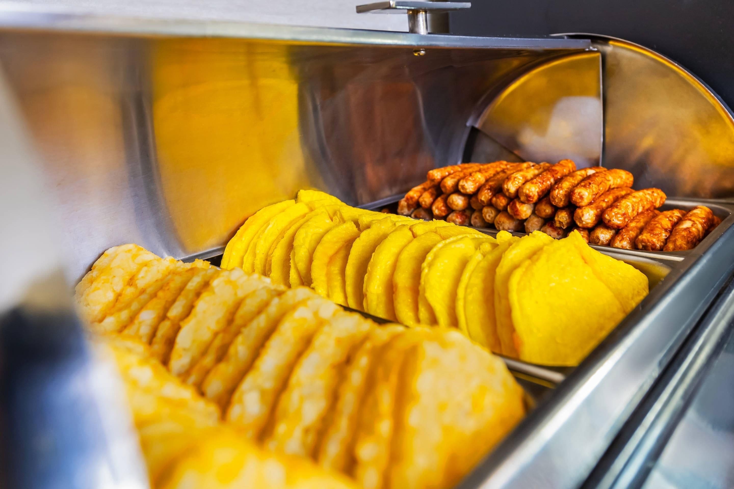 A buffet with sliced yellow fruit and cooked sausages.