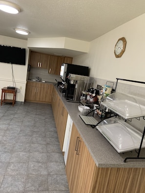 A modern kitchen with wooden cabinets, a stainless steel sink, a coffee machine, and a clock on the wall. - Rodeway Inn (Edson)