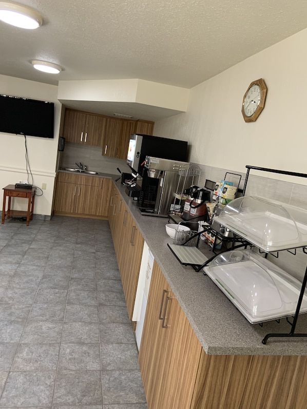 A modern kitchen with wooden cabinets, a stainless steel sink, a coffee machine, and a clock on the wall. - Rodeway Inn (Edson)