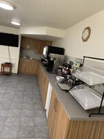 A modern kitchen with wooden cabinets, a stainless steel sink, a coffee machine, and a clock on the wall.