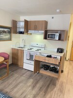 A compact kitchen with wooden cabinets, a built-in microwave, a stove, and a sink.