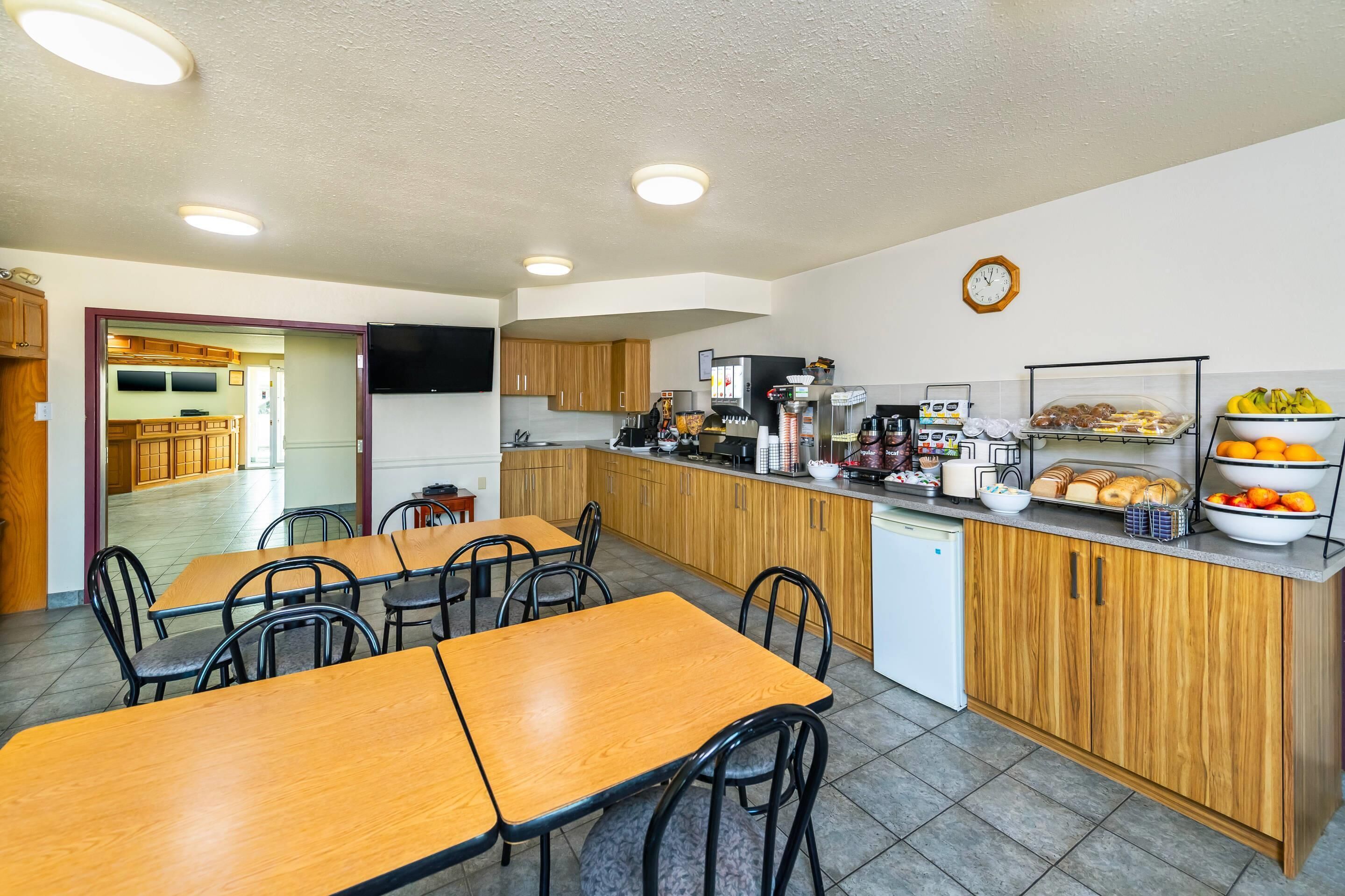 A modern kitchen with wooden cabinets, a coffee machine, and a breakfast bar with fruit and pastries.