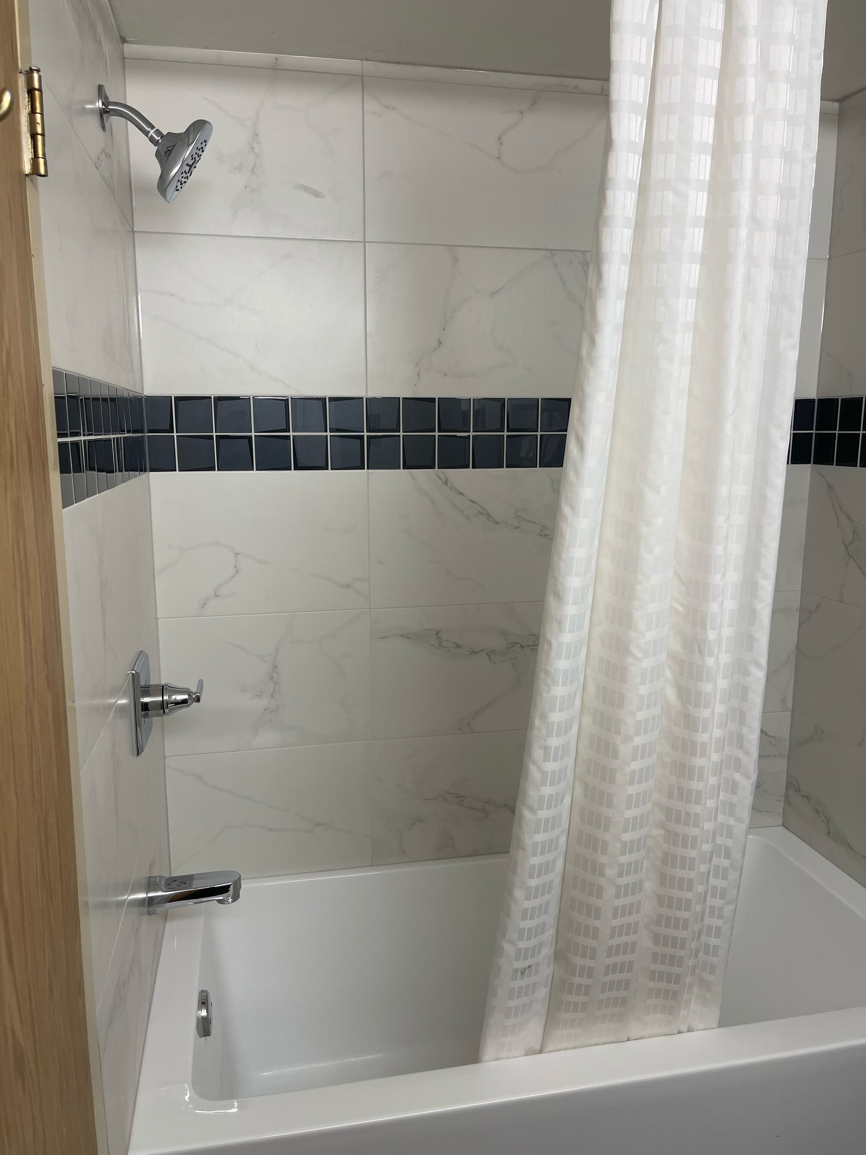 Une salle de bain avec une baignoire, une douche et un mur carrelé agrémenté d’une bande décorative bleue.