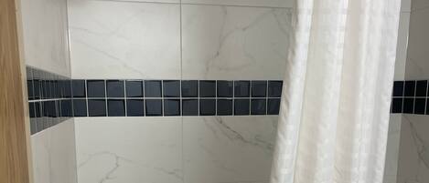 Une salle de bain avec une baignoire, une douche et un mur carrelé agrémenté d’une bande décorative bleue.