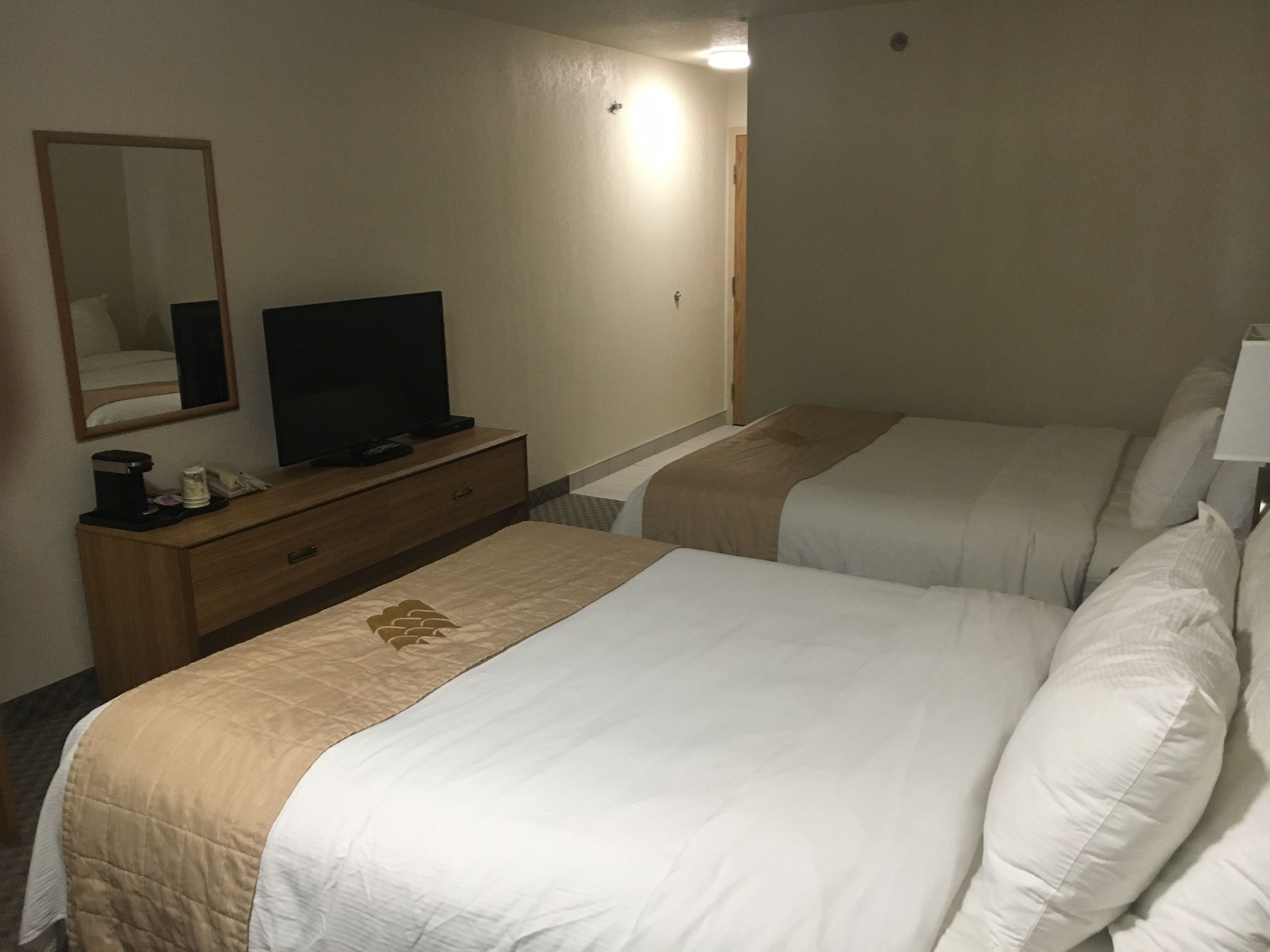 Una camera d'albergo con due letti, una TV su un comò di legno e uno specchio a parete.