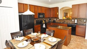A modern kitchen with wooden cabinets, a black refrigerator, a microwave, and a dining area set for four with a table and chairs.