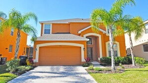 A two-story house with a garage, surrounded by palm trees and a well-maintained lawn.