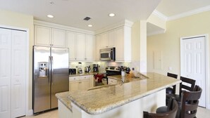 A kitchen with white cabinets, stainless steel appliances, a granite countertop, and a bar area with chairs.