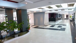 A modern hotel lobby with a geometric floor pattern, a reception desk, and a painting on the wall. - Black Tulip (Dej)