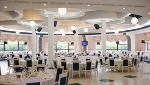 A large banquet hall with round tables set for dining, high ceilings with recessed lighting, and large windows allowing natural light. - Black Tulip (Dej)