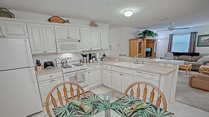Una cocina moderna con armarios blancos, una isla central y una zona de comedor con una mesa y sillas de vidrio.