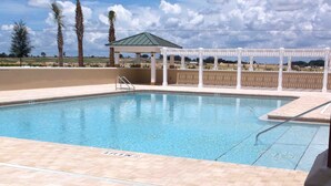 Una piscina con un pérgola blanca y una zona cubierta al fondo.