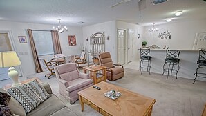 Una sala de estar con sofá, sillón y mesa de centro, un comedor con mesa y sillas, y una cocina con mostrador y taburetes de bar.