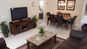 Una sala de estar con televisor, mesa de centro, comedor con sillas y sofá.