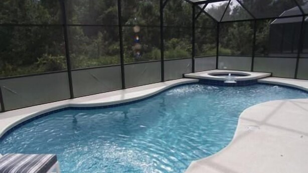 Una piscina con un jacuzzi, rodeada de paredes de vidrio y algunas sillas de descanso.