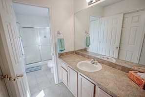 A bathroom with a shower, toilet, sink, and a large mirror.