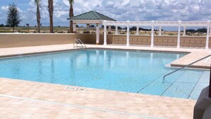 Una piscina con un pérgola blanca y una zona cubierta al fondo.