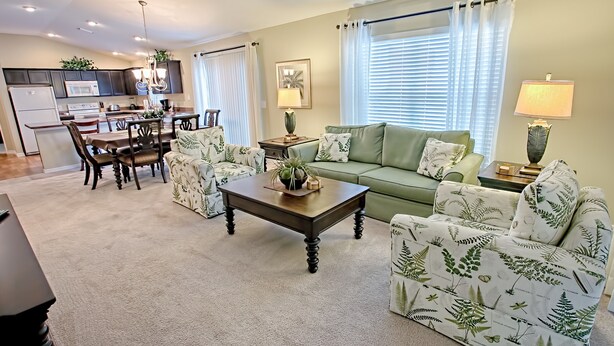 Una sala de estar con un sofá verde, sillones estampados, una mesa de centro y un comedor con mesa y sillas.