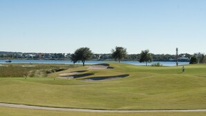 A golf course with bunkers, a water body, and trees.