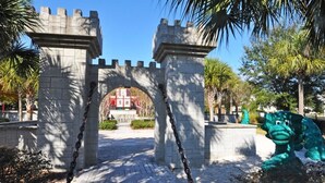 A stone archway with a chain barrier, palm trees, and a green statue.