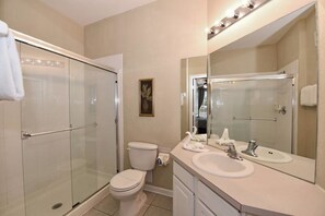 Un baño moderno con ducha de vidrio, inodoro blanco, lavabo con espejo y toallero.