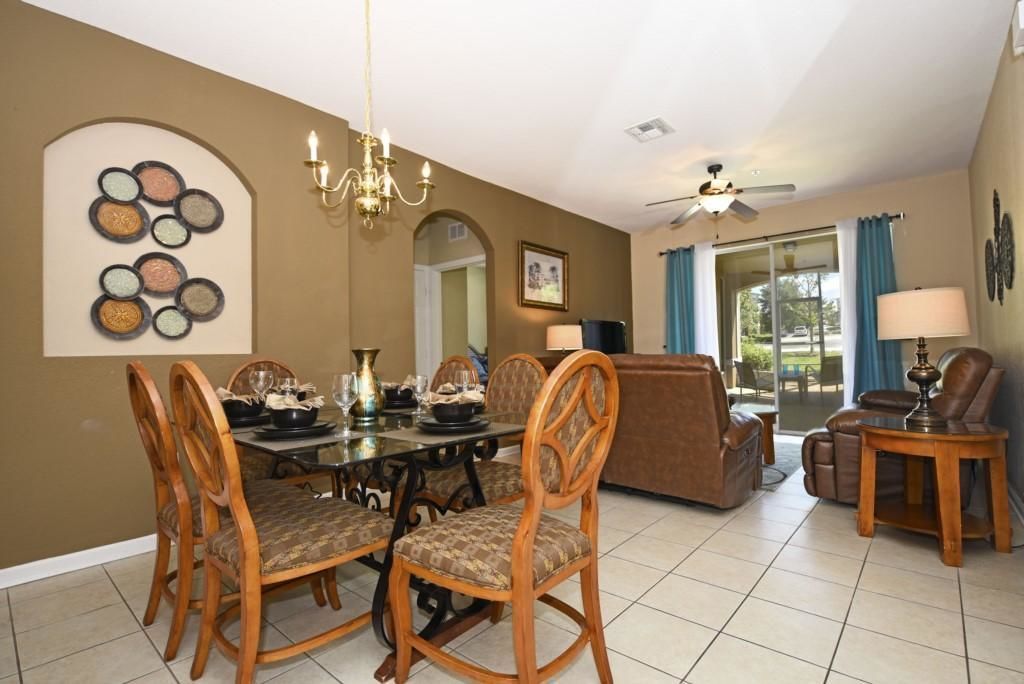A dining area with a chandelier, a dining table set for four, and a sofa with a side table.