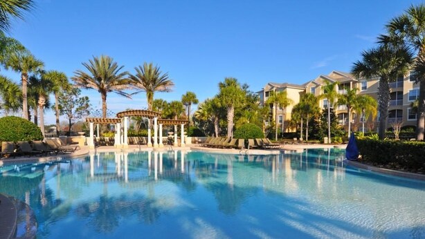 A swimming pool with a gazebo, palm trees, and a building with balconies.
