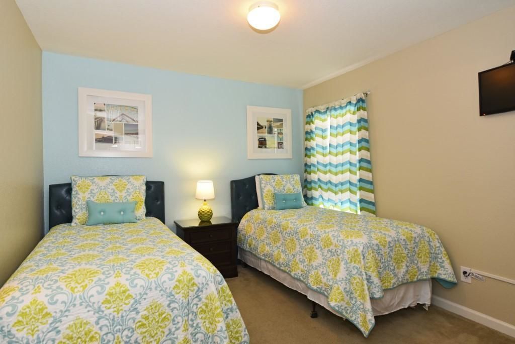 A bedroom with two beds, each with a patterned bedspread, a nightstand with a lamp, and framed pictures on the wall.