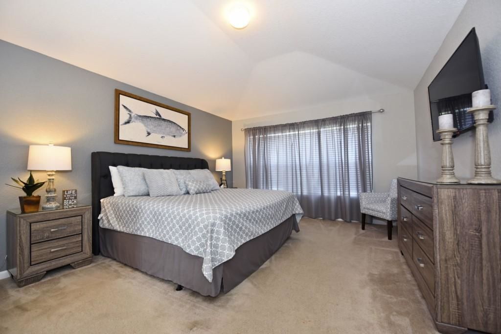 A bedroom with a bed, bedside tables, a chair, a dresser, a television, and a framed picture on the wall.