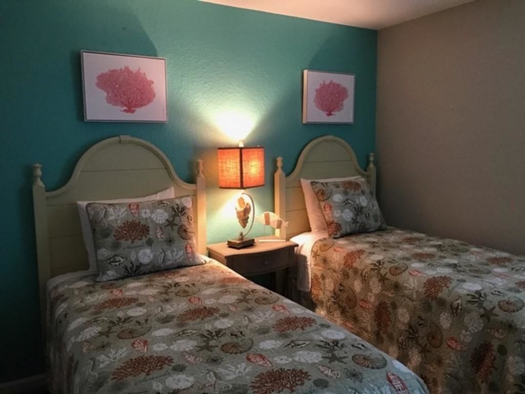 A bedroom with two beds, each with floral bedding, a nightstand with a lamp, and two framed pictures on the wall.