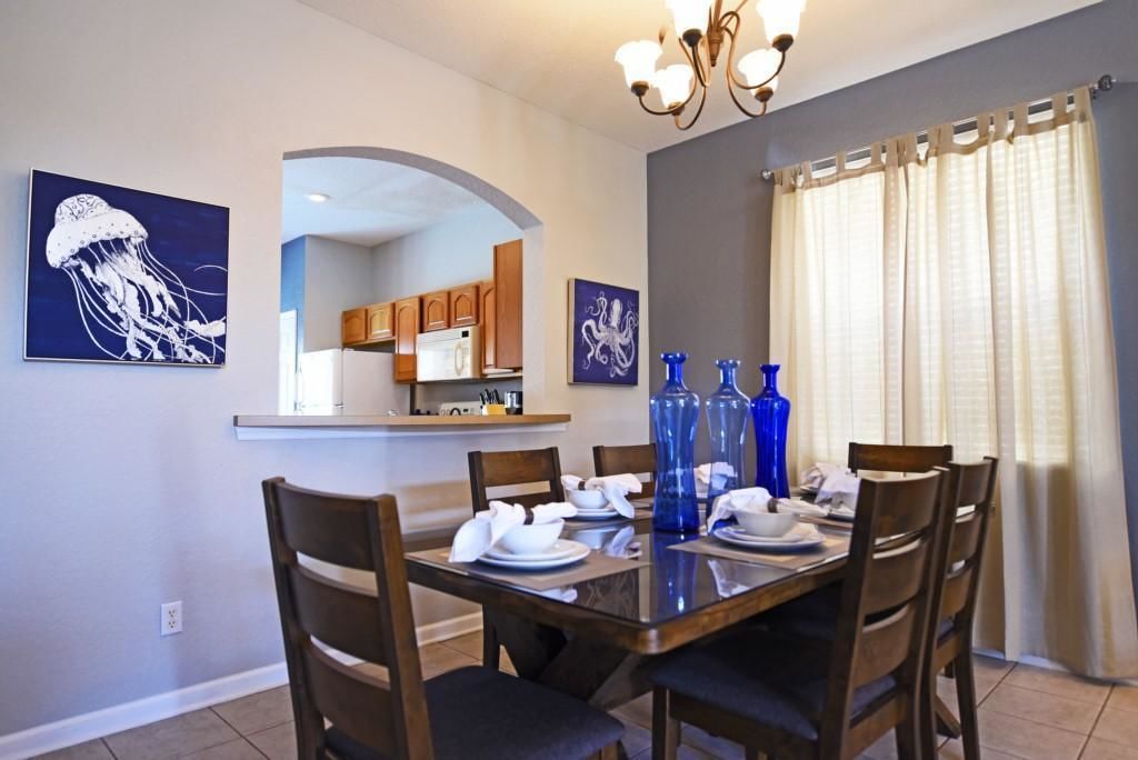 A dining area with a wooden table set for four, surrounded by chairs. There are two blue vases on the table, and artwork on the walls.