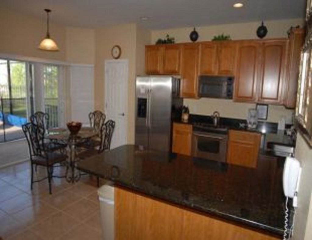 A kitchen with wooden cabinets, a stainless steel refrigerator, a microwave, and a large island with a sink.