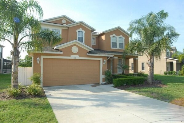 A two-story house with a garage, a driveway, and palm trees. - 820 The Shires House 6 Bedroom by Florida Star (Davenport)